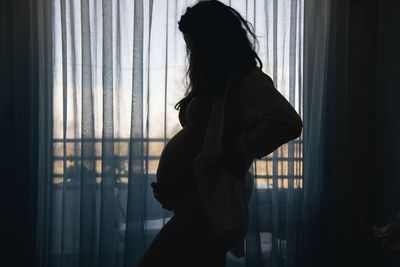 Side view of woman standing by window at home