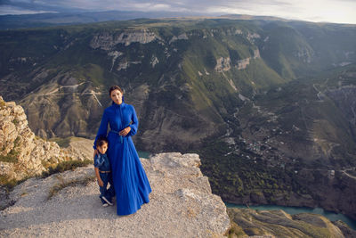 Mother in a blue dress with her son stands on the cliff of the sulak canyon in dagestan
