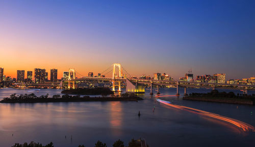 Illuminated bridge over river in city at night