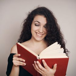 Smiling woman reading book against wall