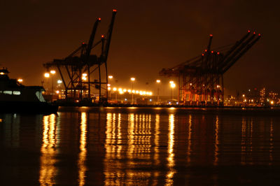 Illuminated commercial dock by river against sky at night