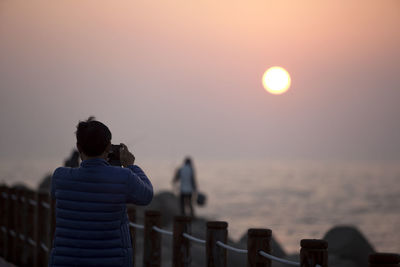 Man photographing on pier at beach during sunset