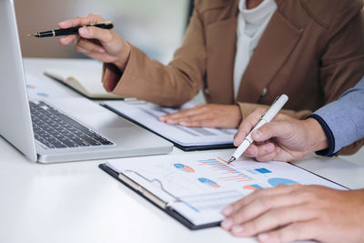 Cropped image of colleagues using laptop with graph papers in office