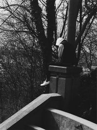 Woman sitting on bare tree against sky