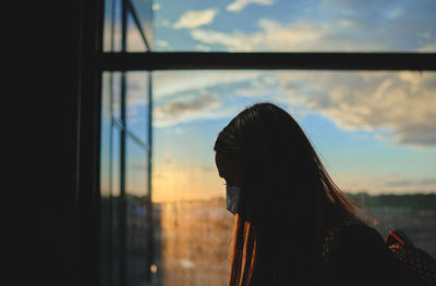 View on the aiport window with woman walking with suitcase at the departure hall during the sunset. 