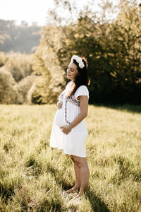 Smiling pregnant woman with eyes closed standing on grassy field