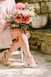 Low section of woman holding bouquet while sitting on chair