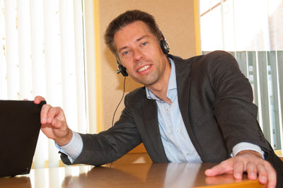 Portrait of businessman using headphones against wall