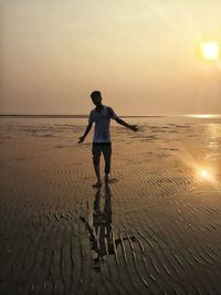 Full length of man standing on beach against sky during sunset