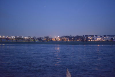 Illuminated city by sea against clear sky at night