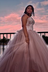 Portrait of young woman standing against sky during sunset
