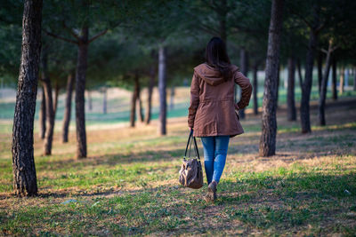 Rear view of woman walking on grass in forest