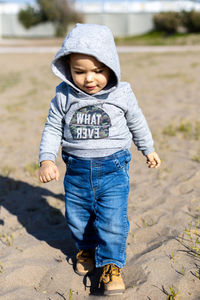 Sweet baby boy in hoodie and jeans walking and playing in the sand. activity with toddler.