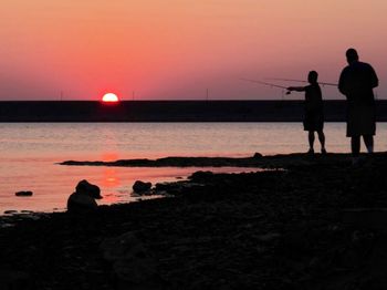Silhouette of people standing on beach at sunset