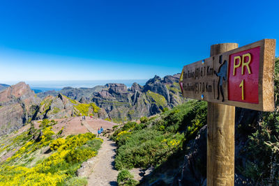 Road sign by mountain against blue sky