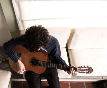 High angle view of man playing guitar while sitting on sofa at home