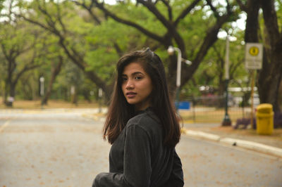 Portrait of young woman standing against trees at park