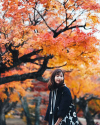 Portrait of young woman standing by tree during autumn