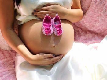  pregnant girl hands touching stomach holding pink shoes