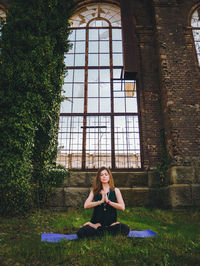 Woman meditating on field against large window
