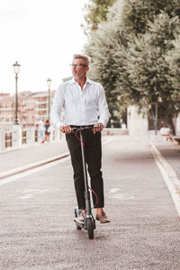 Young businessman in a suit riding an electric scooter while commuting to work in city.