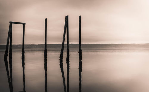 Wooden posts in lake against sky