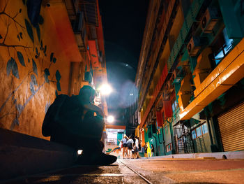 People walking on illuminated street amidst buildings at night