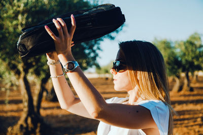 Side view of woman shielding eyes while standing at olive orchard