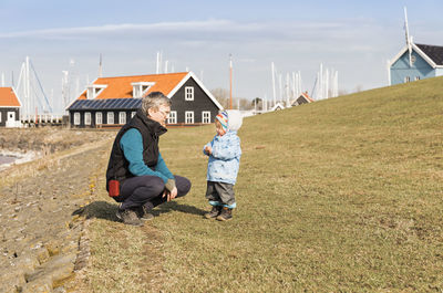 Side view of grandfather and daughter on grass against sky