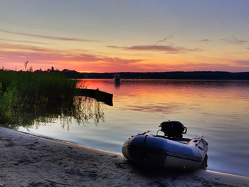 Inflatable raft moored at riverbank against sky during sunset