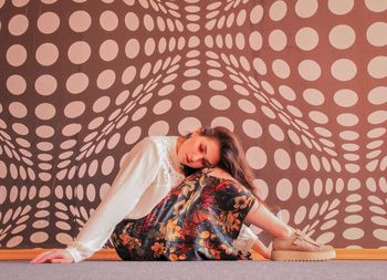 Side view of woman sitting on floor against patterned wall