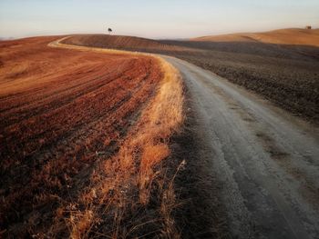 Dirt road on field against sky