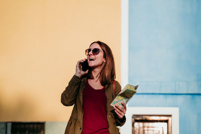 Young woman using mobile phone while standing against wall
