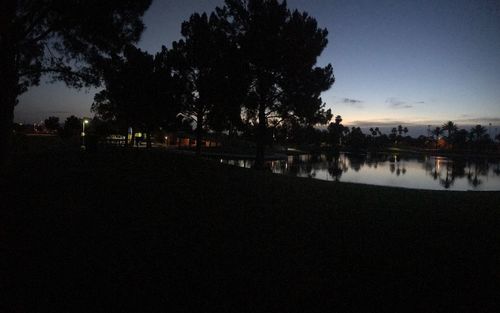 Reflection of silhouette trees in lake against sky