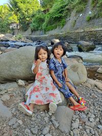 Portrait of sisters sitting on rock by river