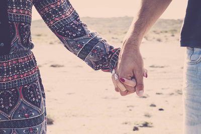 Midsection of couple with holding hands standing at beach