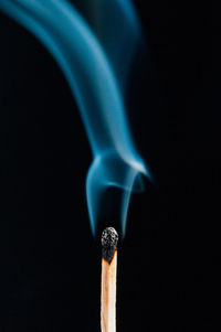 Close-up of burnt matchstick with smoke against black background