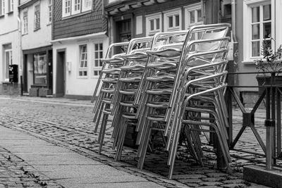 Empty chairs on sidewalk by street against buildings in city