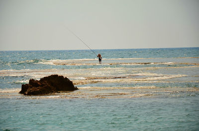 Man fishing in sea against clear sky