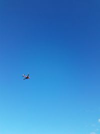 Low angle view of airplane flying against clear blue sky