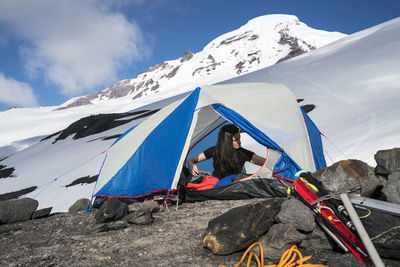A woman reaches for something while she sits in her tent at base camp, mt. baker