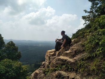 Man sitting on rock looking at mountains against sky