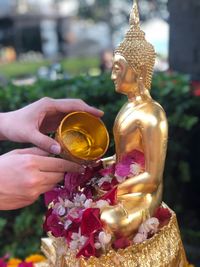 Cropped hands of woman pouring water on flowers and statue