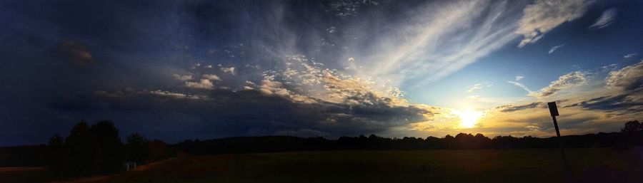 Silhouette trees on field against dramatic sky during sunset