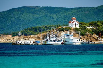 Boats moored in blue water against lush foliage