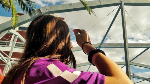 Low angle view of woman shielding eyes while looking at cloudy sky on sunny day