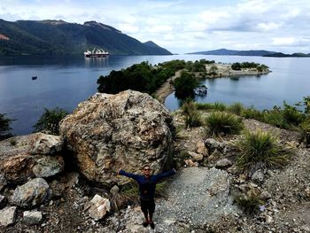 Man standing on rock by lake against sky