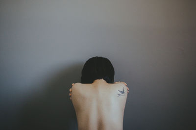 Rear view of shirtless woman against gray wall