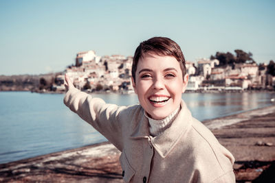 The woman with short hair is smiling and pointing to the village overlooking the lake. 