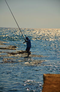 Man fishing in sea against clear sky